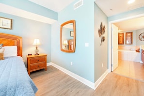A bedroom with a bed, bedside table, lamp, and a large mirror. - Sanibel Condo #302 3/3 Direct Oceanfront NE Corner (Daytona Beach Shores)