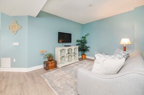 A living room with a light blue wall, a white cabinet, a grey sofa, a TV, a floor lamp, and a potted plant.