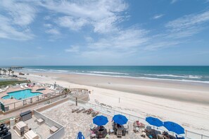 A beach view with a pool, lounge chairs, and umbrellas. - Sanibel Condo #302 3/3 Direct Oceanfront NE Corner (Daytona Beach Shores)