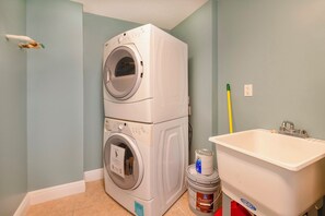 A laundry room with stacked washers and dryers, a sink, and a bucket of detergent. - Sanibel Condo #302 3/3 Direct Oceanfront NE Corner (Daytona Beach Shores)