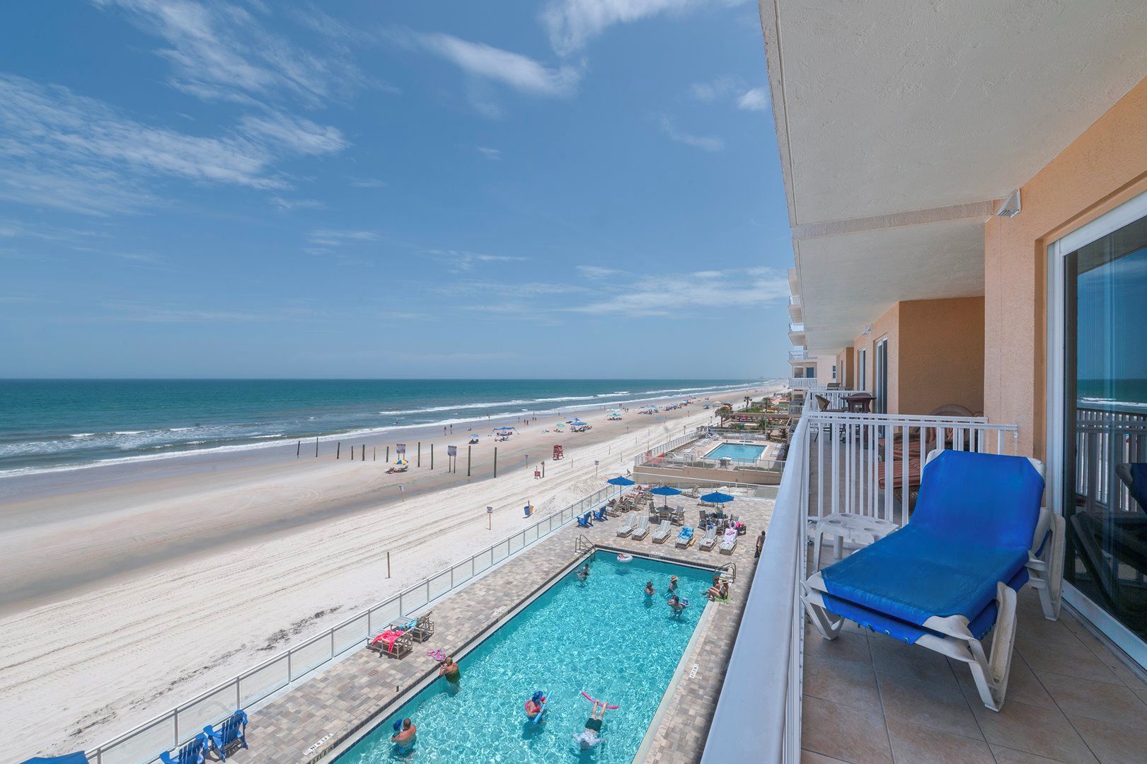 A balcony with a pool, beach view, and lounge chairs.