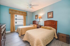 A hotel room with two beds, a ceiling fan, a window with curtains, and a dresser.