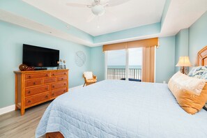 A bedroom with a large bed, a dresser, a television, and a view of the ocean through a balcony. - Sanibel Condo #302 3/3 Direct Oceanfront NE Corner (Daytona Beach Shores)