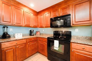A kitchen with wooden cabinets, a black microwave, a stove, a blender, and a coffee maker.