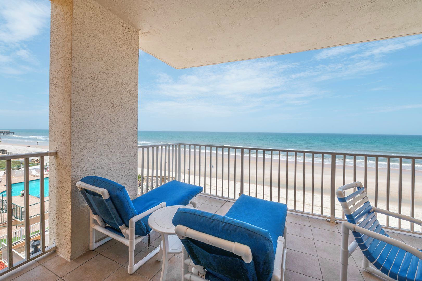 Un balcon avec deux fauteuils et une petite table, donnant sur une plage et une piscine.