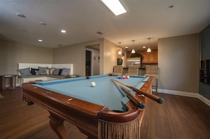 A pool table in a room with a sofa and a kitchen area in the background. - Sanibel Condo #302 3/3 Direct Oceanfront NE Corner (Daytona Beach Shores)