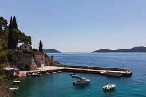 A coastal town with a historic stone building, a clear blue sea, and several boats docked at a pier. - Apartment Pod Nespolom (Dubrovnik)