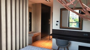 A modern bedroom with a bed, a desk, and a chair. There is a window with a view of buildings and trees. - Apartament Dzielna 64 (Warsaw)