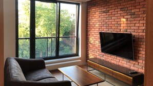 A modern living room with a large window, a brick wall, and a flat-screen TV. - Apartament Dzielna 64 (Warsaw)