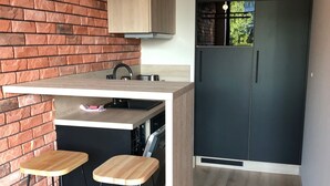 A modern kitchen with a brick wall, wooden bar stools, a built-in oven, and a black refrigerator. - Apartament Dzielna 64 (Warsaw)