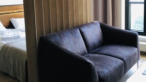 A modern hotel room with a dark brown sofa, a wooden partition, a bed with white bedding, and a large window with curtains. - Apartament Dzielna 64 (Warsaw)