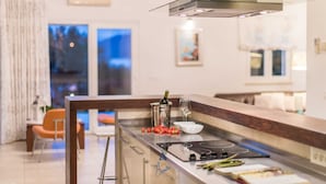 A modern kitchen with a central island, stainless steel appliances, and a view of the living area. - Luxury 6-BR Waterfront Villa with Infinity Pool and direct access to a pebble beach (Supetar)