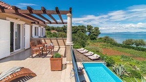 A balcony with a pool, wooden furniture, and a view of the sea. - Luxury 6-BR Waterfront Villa with Infinity Pool and direct access to a pebble beach (Supetar)
