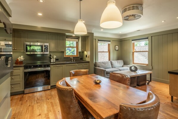 A modern kitchen with a dining area, wooden flooring, and pendant lighting. - Cedar Crest Cottage Near Homewood (Homewood)