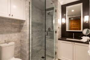 A modern bathroom with a glass-enclosed shower, marble tiles, a dark countertop, and white cabinets. - Cedar Crest Cottage Near Homewood (Homewood)