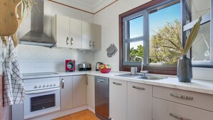 A modern kitchen with white cabinets, a stainless steel range hood, a dishwasher, and a window with a view of trees.