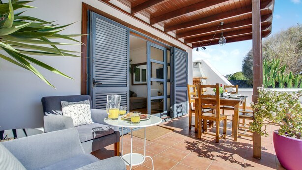 An outdoor patio with a sofa, table, and chairs, a potted plant, and a wooden pergola.