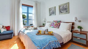 A neatly arranged bedroom with a bed, bedside tables, a sofa, and a window with curtains.