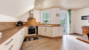 A modern kitchen with wooden cabinets, a built-in oven, and a window with a view. - Cozy Top-Floor Apartment "Vogelsang" with Mountain View, Wi-Fi & Balcony (Herdwangen-Schönach)