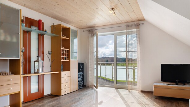 A modern living room with a large window, wooden flooring, and built-in shelving. - Cozy Top-Floor Apartment "Vogelsang" with Mountain View, Wi-Fi & Balcony (Herdwangen-Schönach)