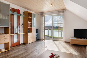A modern living room with a large window, wooden flooring, and built-in shelving.