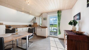 A modern kitchen with a wooden ceiling, a dining table with chairs, a kitchen island, and a view through a glass door. - Cozy Top-Floor Apartment "Vogelsang" with Mountain View, Wi-Fi & Balcony (Herdwangen-Schönach)