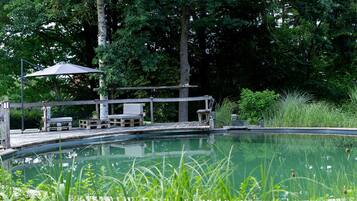 Uma piscina com deck de madeira, espreguiçadeiras e toldo.