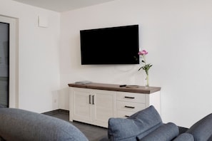 Una sala de estar moderna con un televisor de pantalla plana montado en la pared, un mueble de madera con cajones y un florero con flores sobre el mueble.