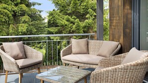 Un balcon agrémenté de meubles en osier, d’une table en verre et offrant une vue sur les arbres.