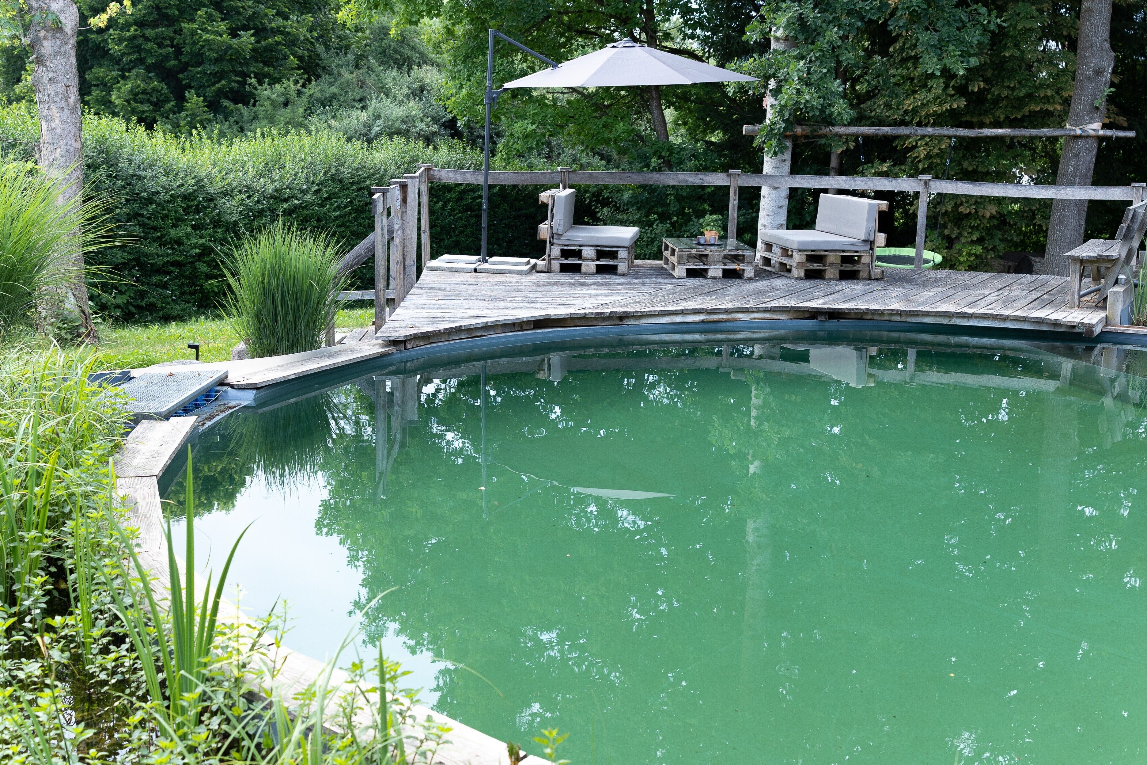 Una terrazza in legno con piscina, immersa nel verde.