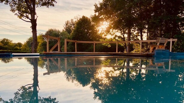 A swimming pool with a wooden deck and trees in the background. - Holiday Apartment "Bodensee" with Terrace, Shared Garden & Swimming Pond (Meßkirch)