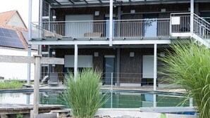 A multi-story building with balconies, a swimming pool, and surrounding vegetation. - Holiday Apartment "Bodensee" with Terrace, Shared Garden & Swimming Pond (Meßkirch)
