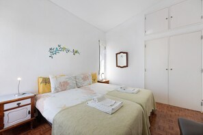 Une chambre avec deux lits, une table de chevet, une commode, une armoire et un miroir au mur.