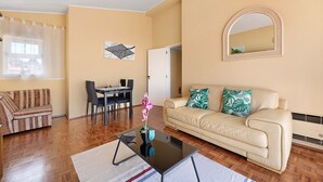 Un salon comprenant un canapé, une table basse, un coin repas avec des chaises, un miroir et une fenêtre avec des rideaux.