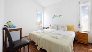 Une chambre avec deux lits, une chaise, une commode en bois, une fenêtre et un élément décoratif mural.