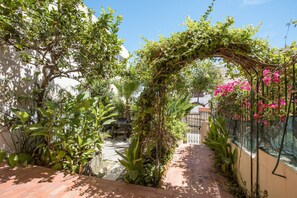 A garden pathway with a wooden bench, surrounded by lush greenery and flowering plants. - Pet-Friendly Studio with Private Garden & Wi-Fi (Lagos)