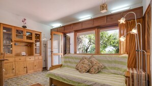 A cozy room with a sofa, wooden cabinets, a dining table, and a window with curtains. - Pet-Friendly Studio with Private Garden & Wi-Fi (Lagos)