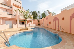 A swimming pool with a curved edge, surrounded by a pink building with balconies and a palm tree. - Holiday Apartment "Ibn Sadi 8 Playa Burriana" Close to the Beach with Terrace (Nerja)