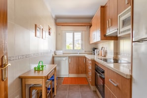 A compact kitchen with wooden cabinets, a dishwasher, a microwave, and a window providing natural light.
