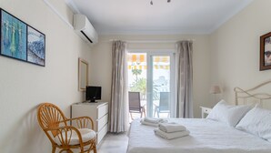 Ein Hotelzimmer mit Bett, Sessel, Schreibtisch, Fernseher und einem Balkon mit Vorhängen.