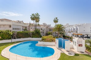 Una piscina de borde curvo, rodeada por una valla blanca y palmeras.