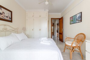 Une chambre à coucher comprenant un lit, une chaise, un ventilateur de plafond et une porte donnant sur une autre pièce.