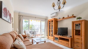 Ein Wohnzimmer mit Sofa, Fernseher, Holzschrank und einem Balkon mit Tisch und Stühlen.