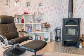 A living room with a black leather chair, a white bookshelf, a black wood-burning stove, and patterned wallpaper.