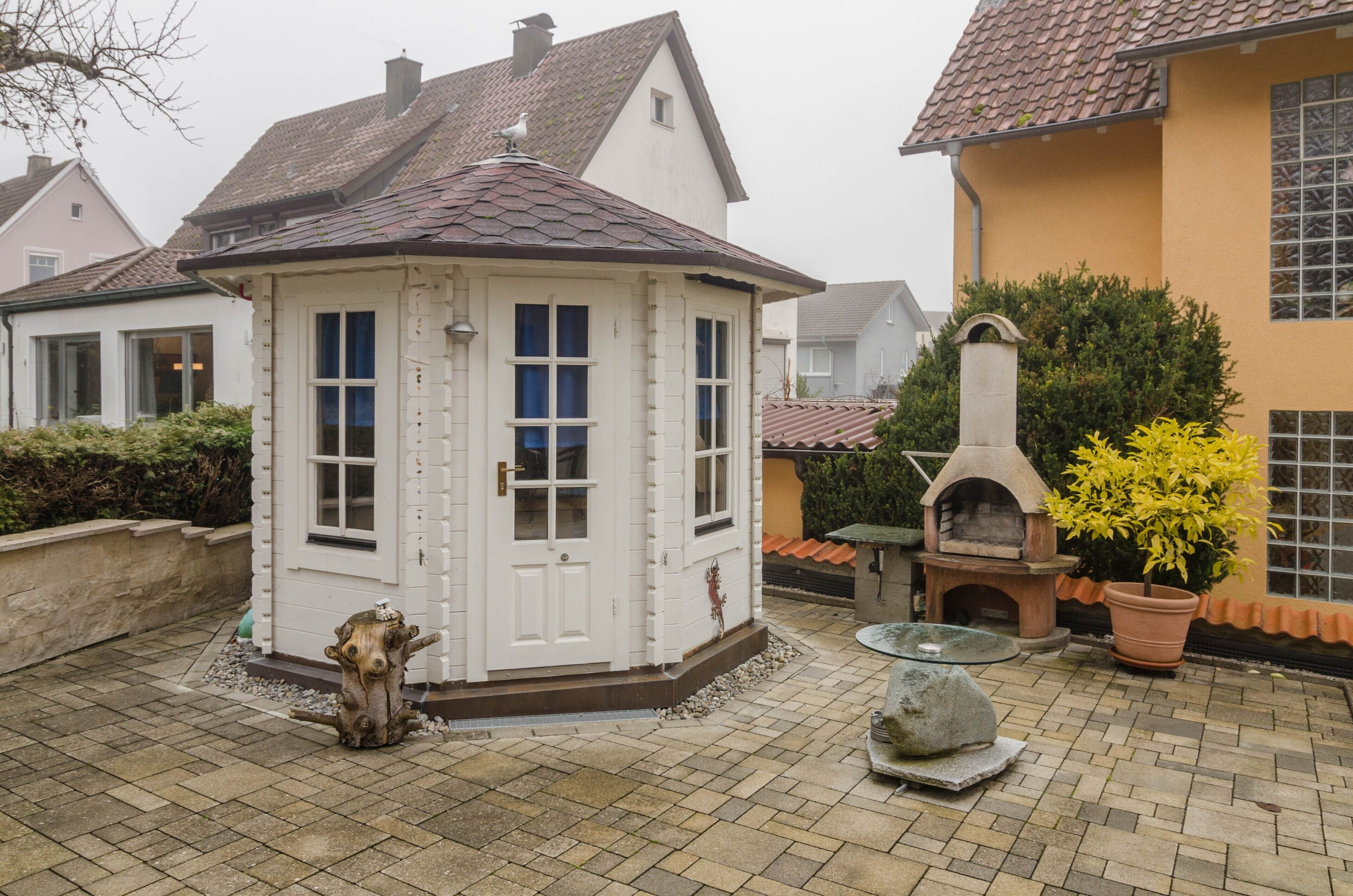 Ein weißes Gebäude mit einem Ziegeldach, einem Steinkamin und einem Blumentopf.