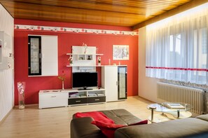 A living room with a red wall, white furniture, a glass coffee table, and a television.