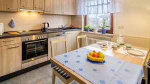A modern kitchen with wooden cabinets, a stove, and a dining table set with a fruit bowl and plates. - Holiday Apartment Kramer with Wi-Fi, Terrace & Shared Garden (Überlingen)