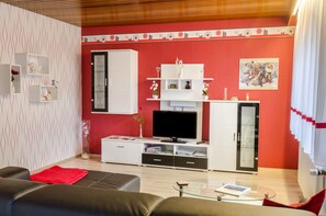 A modern living room with a red accent wall, white furniture, a television, and decorative items.