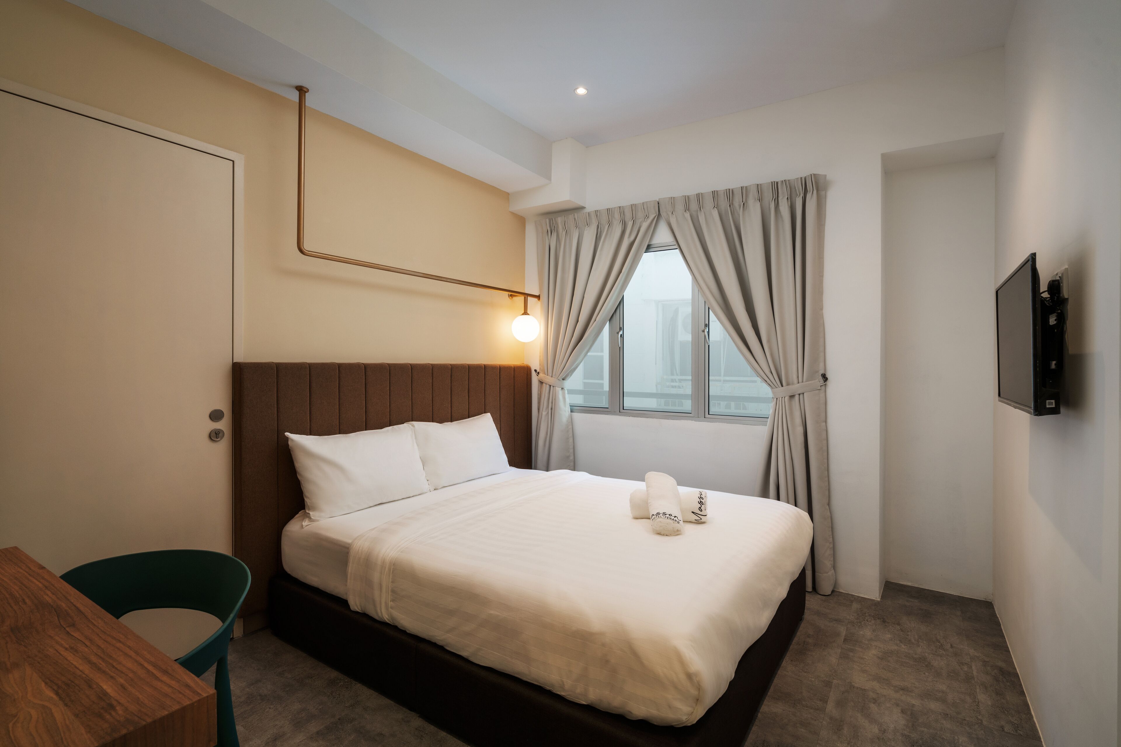 Une chambre d’hôtel avec un lit, un bureau, une chaise, une télévision et une fenêtre avec des rideaux.