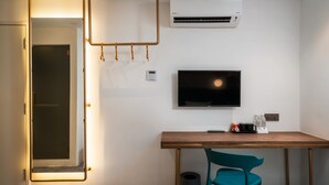 Une chambre moderne avec un bureau en bois, une chaise de couleur turquoise, un téléviseur fixé au mur et un appareil de climatisation.